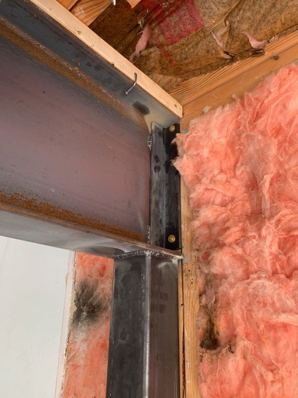 A close up of a metal beam in a room with pink insulation.