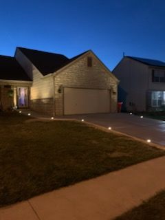 A suburban house exterior at dusk, illuminated by small solar path lights lining the edge of the driveway.