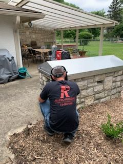 A man wearing headphones is kneeling down in front of a brick wall.