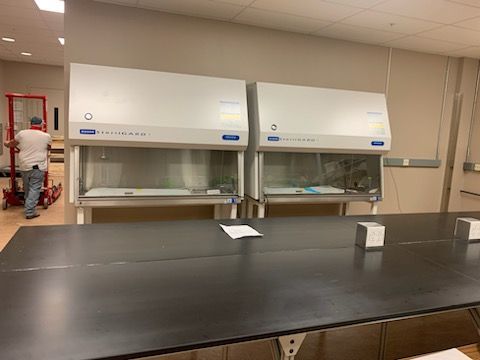 A man is pushing a dolly in a lab next to a table.