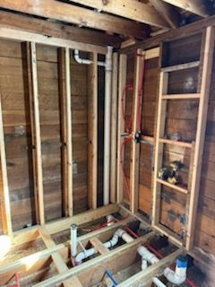 Framed bathroom walls with exposed white PVC plumbing pipes and red PEX water lines in an unfinished wood structure.