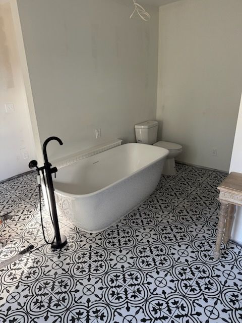 Bathroom with black and white patterned floor, white freestanding tub, and black faucet.
