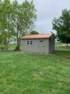 A small shed with a red roof is sitting in the middle of a lush green field.