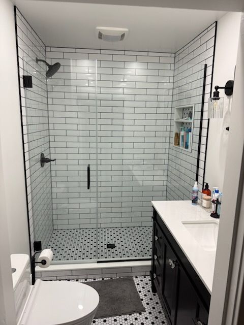 Modern bathroom with white subway tile shower, black accents, and black and white patterned floor.