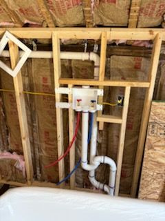 Wall cavity showing a washing machine outlet box with red and blue water lines, white drain piping, and insulation.