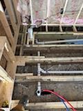 Interior view of floor framing with gray PVC plumbing pipes and red and blue PEX water lines installed between joists.