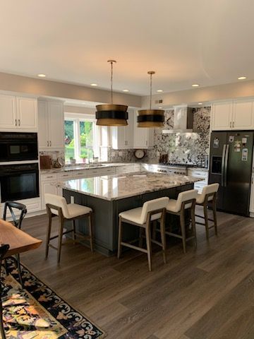 A kitchen with a large island , stools , a table and a refrigerator.