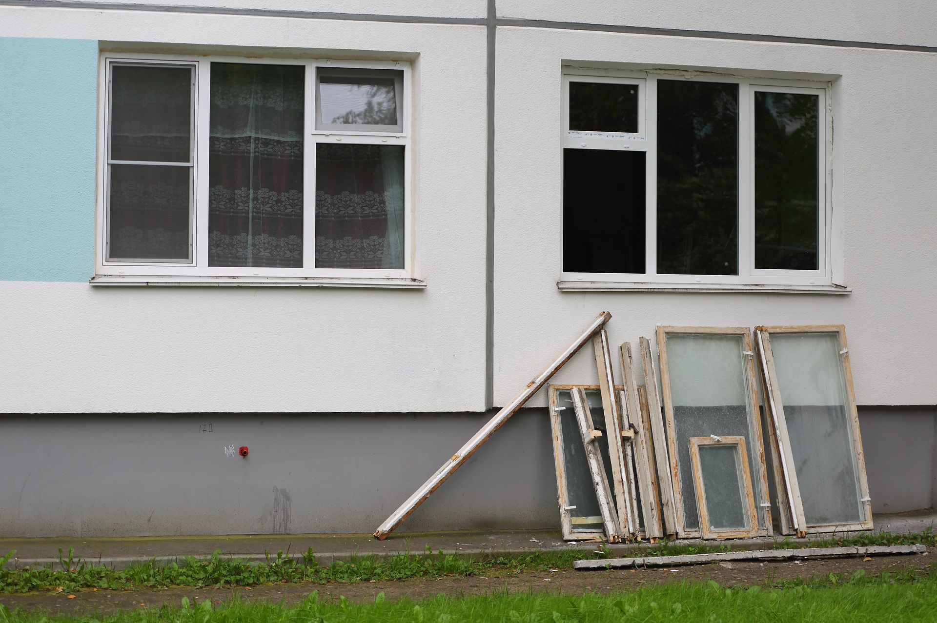 Exterior of building with white-framed windows, some removed and leaning against the wall.