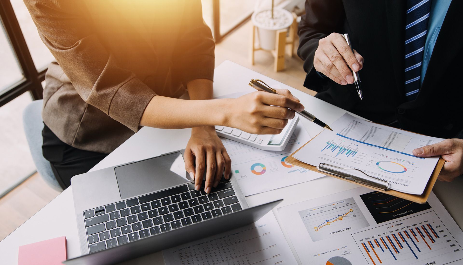 Two people reviewing financial charts with a laptop and calculator at a desk.