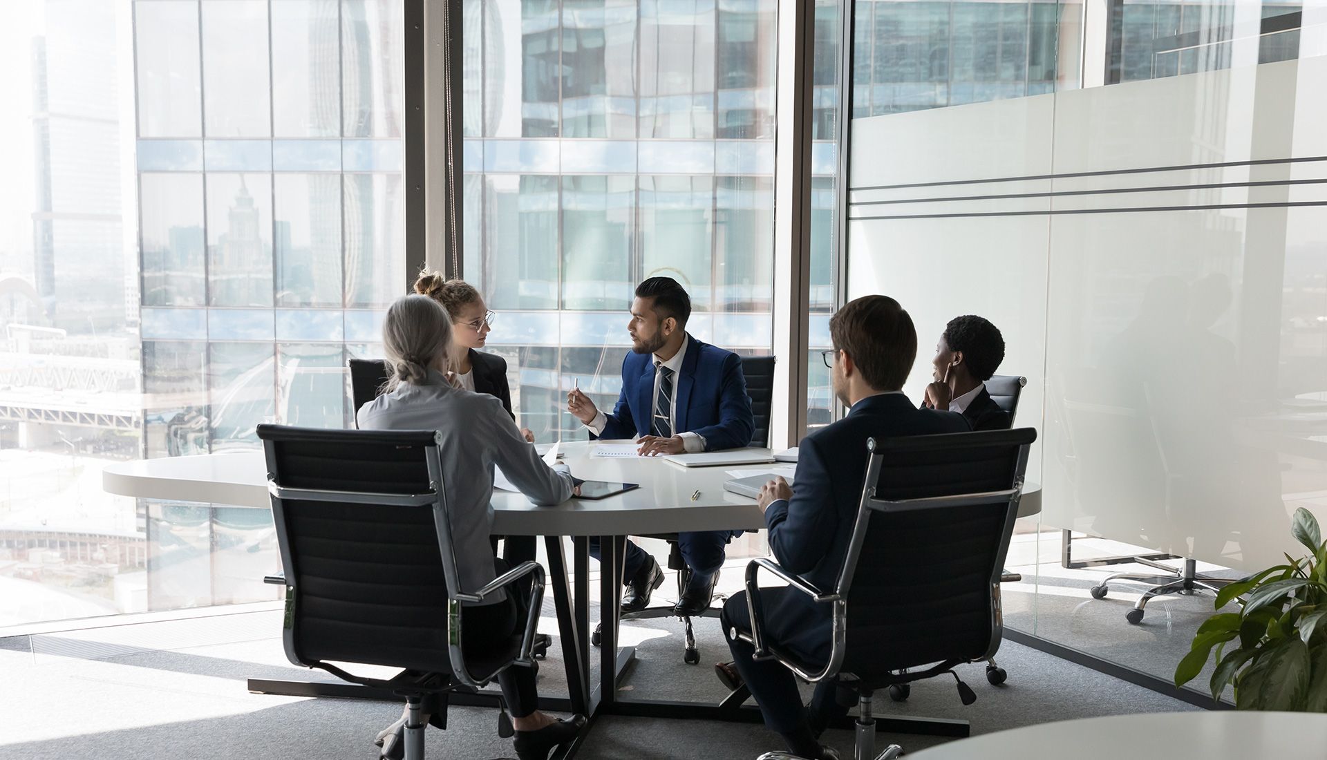 People in business attire at a conference table with city view through large windows.