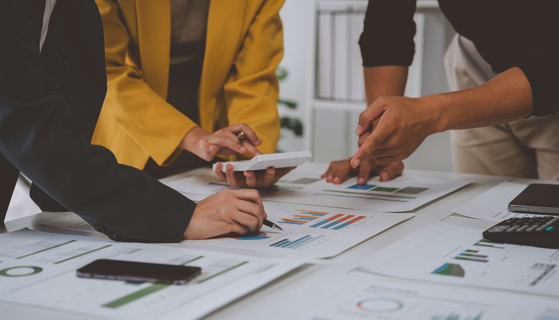 People reviewing charts and using a calculator, in an office setting.