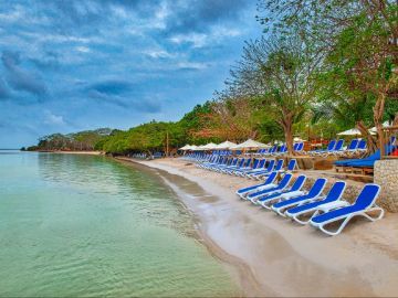 Playa con hileras de tumbonas azules frente a aguas turquesas bajo un cielo nublado.