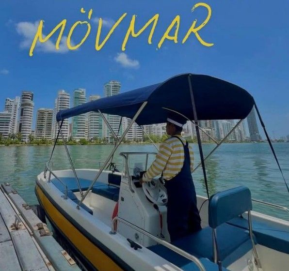 Un operador de barco dirige una lancha motora con toldo azul frente al horizonte de la ciudad en un día soleado.