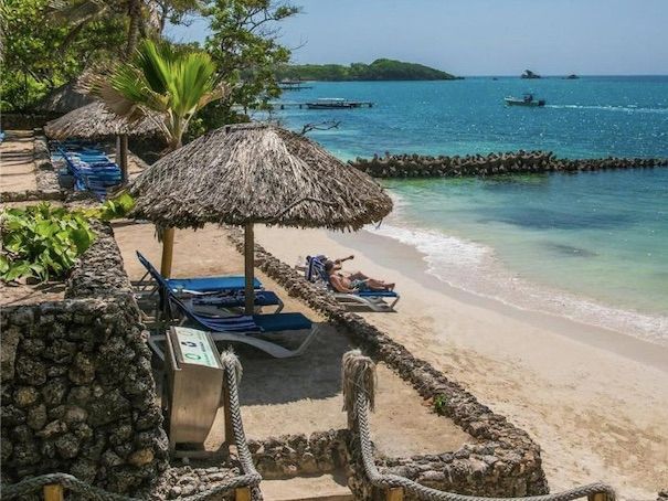 Playa con orilla arenosa, tumbonas, sombrillas de paja y agua cristalina de color turquesa.