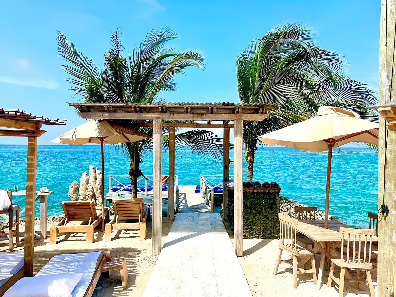 Escena de playa con estructuras de madera, sombrillas y vistas al océano.