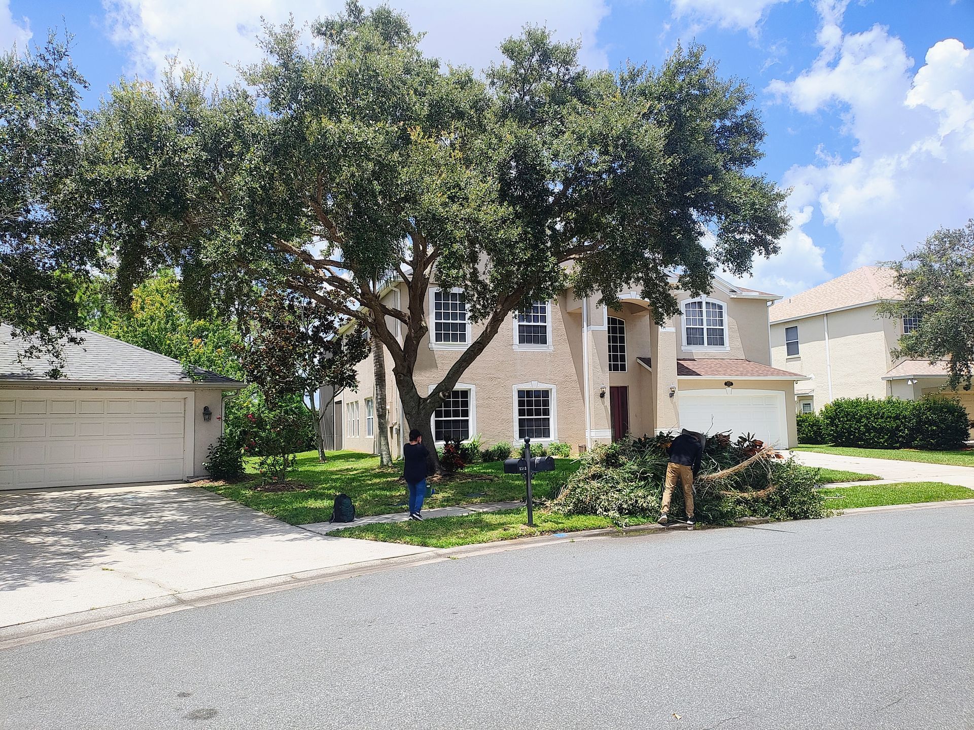 A man is cutting a tree in front of a house.