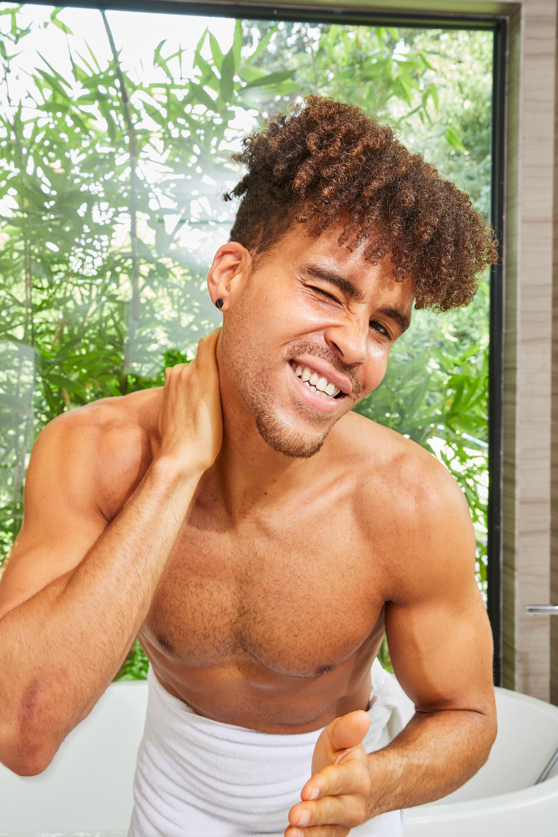 A shirtless man is sitting in a bathtub with a towel around his neck.