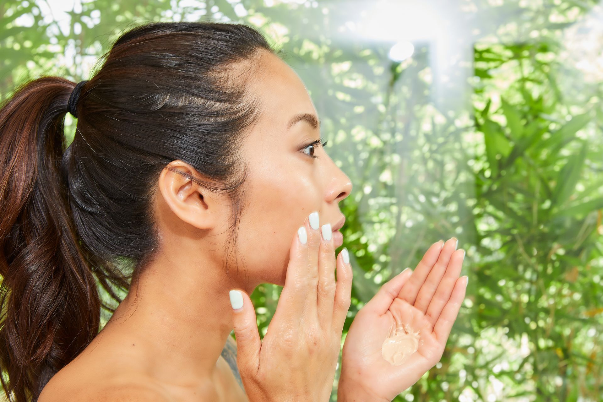 A woman is applying lotion to her face.