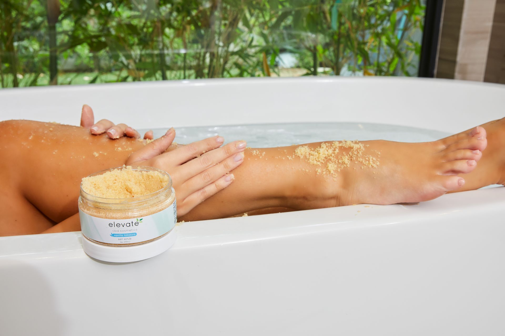 A woman is taking a bath with a jar of body scrub next to her.