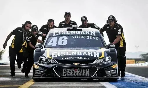 Um grupo de homens está empurrando um carro de corrida em uma pista.