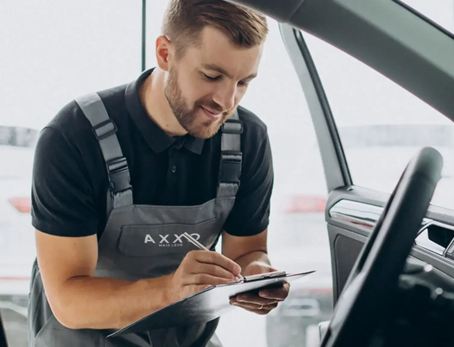 Um homem de macacão está olhando para uma prancheta em um carro.