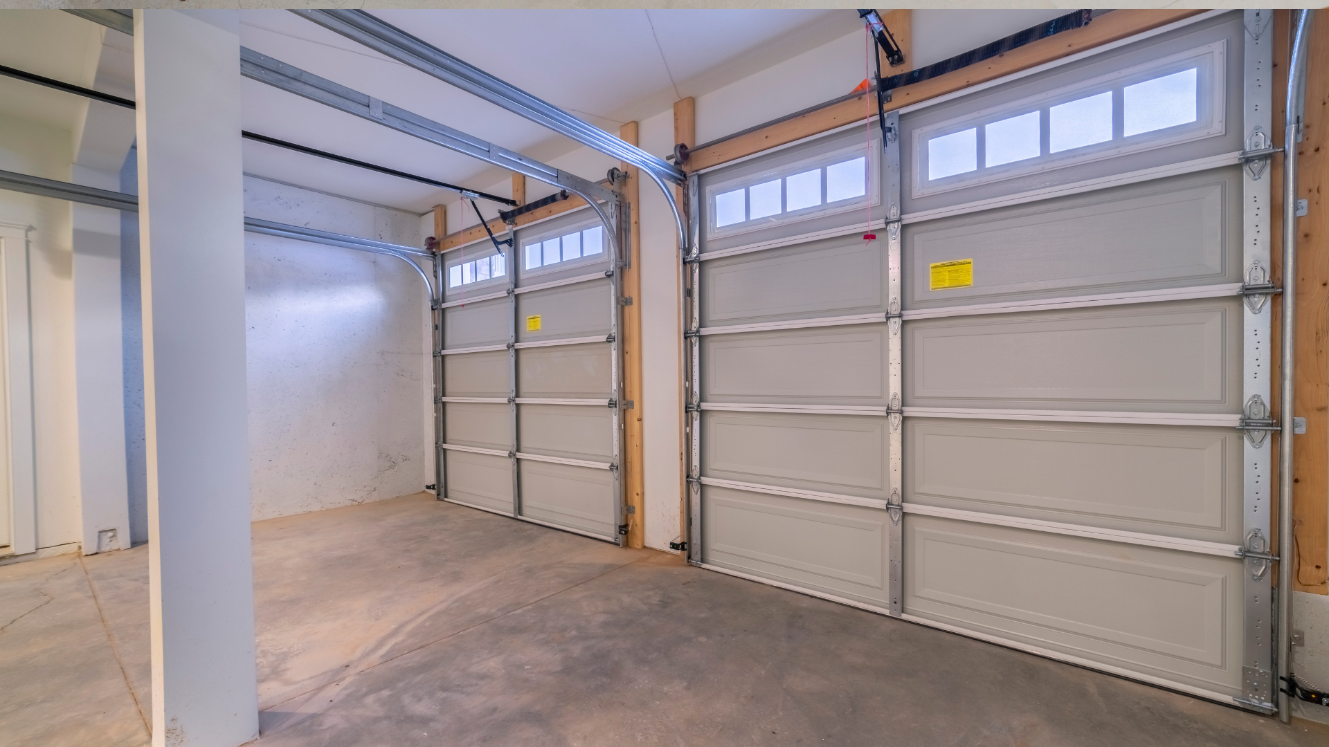 An interior view of a garage featuring two closed white sectional garage doors with top row windows.