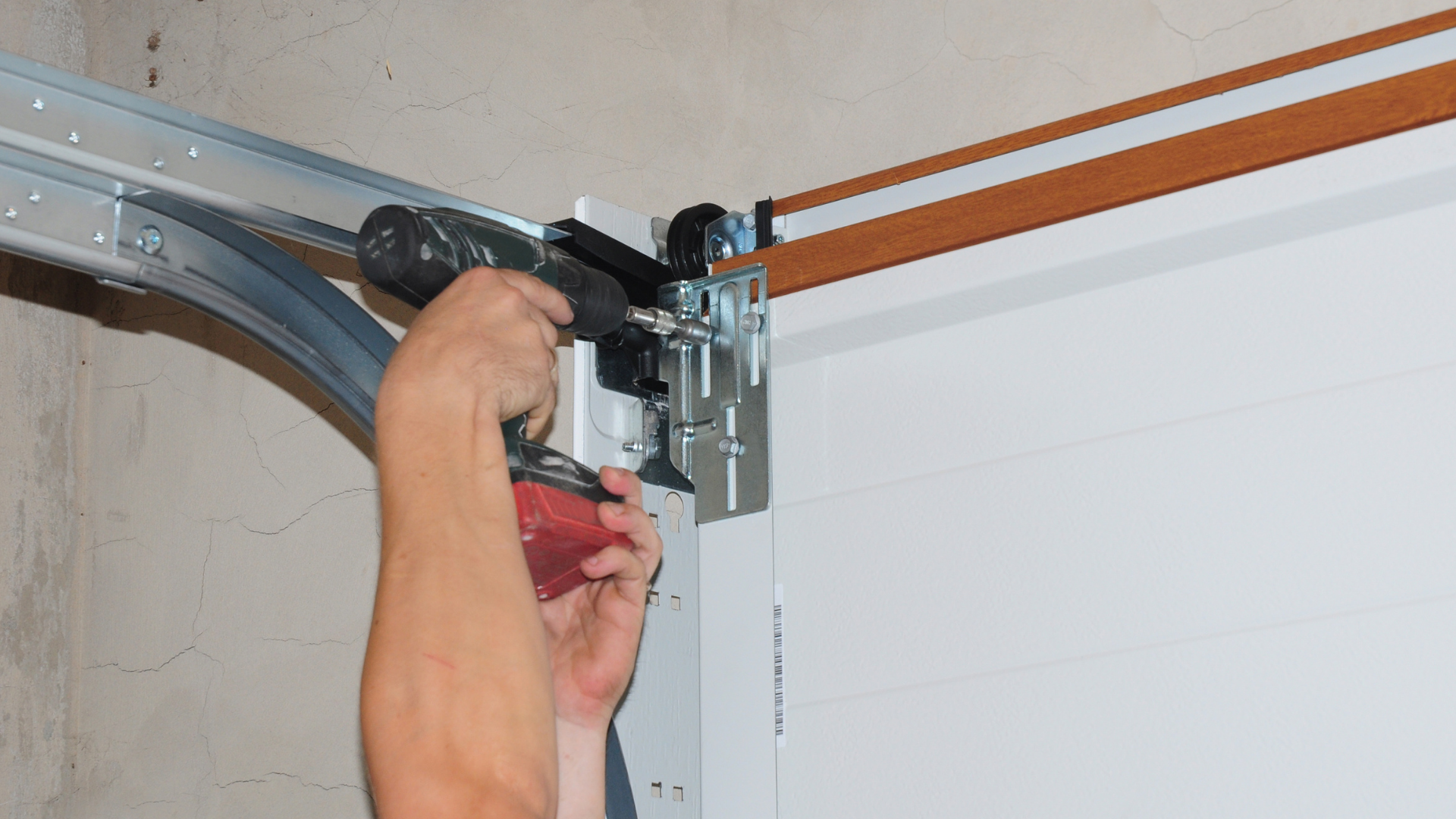A person using a cordless power drill to secure hardware onto a white garage door panel.