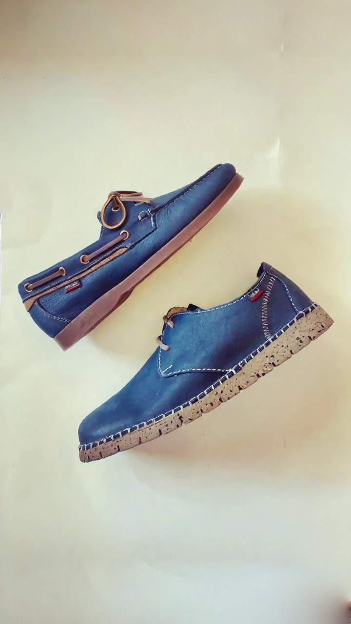 Due paia di scarpe in pelle blu su sfondo neutro. Le scarpe hanno la suola marrone.