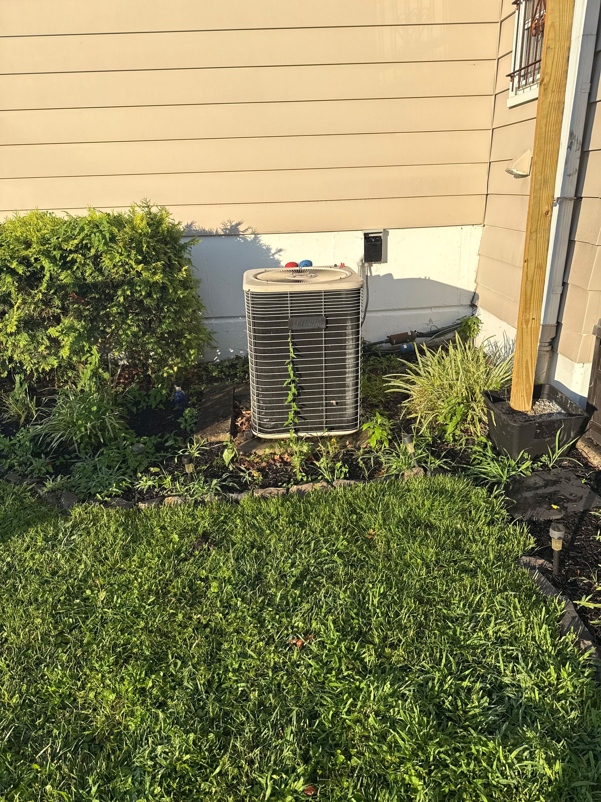 Outdoor air conditioning unit surrounded by overgrown greenery, near a house.