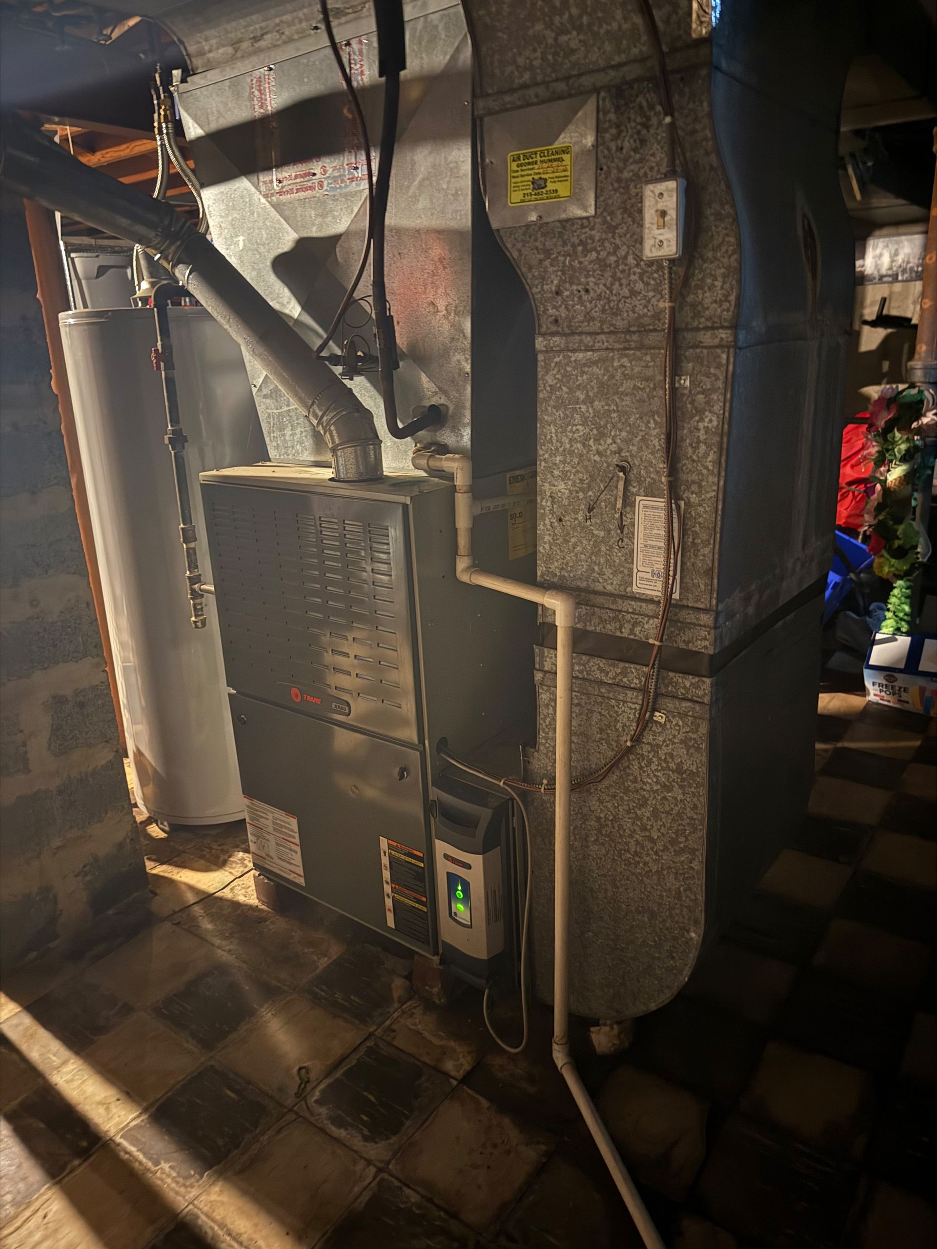 Furnace and ductwork in a basement. Grey metal unit with connected pipes.