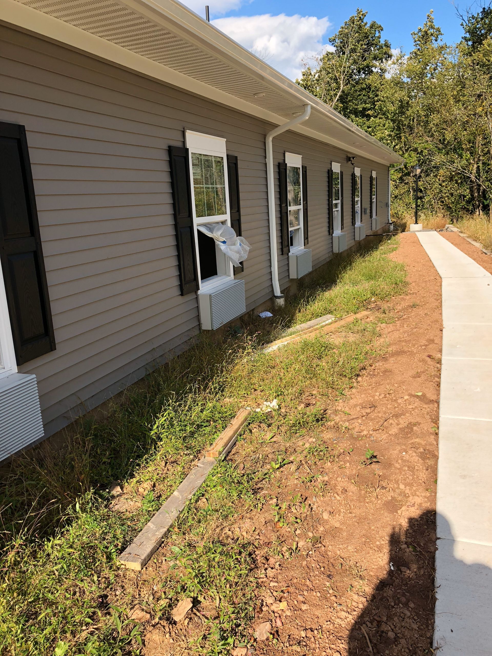 A building with multiple windows; one window has a broken air conditioning unit. A sidewalk is to the right.