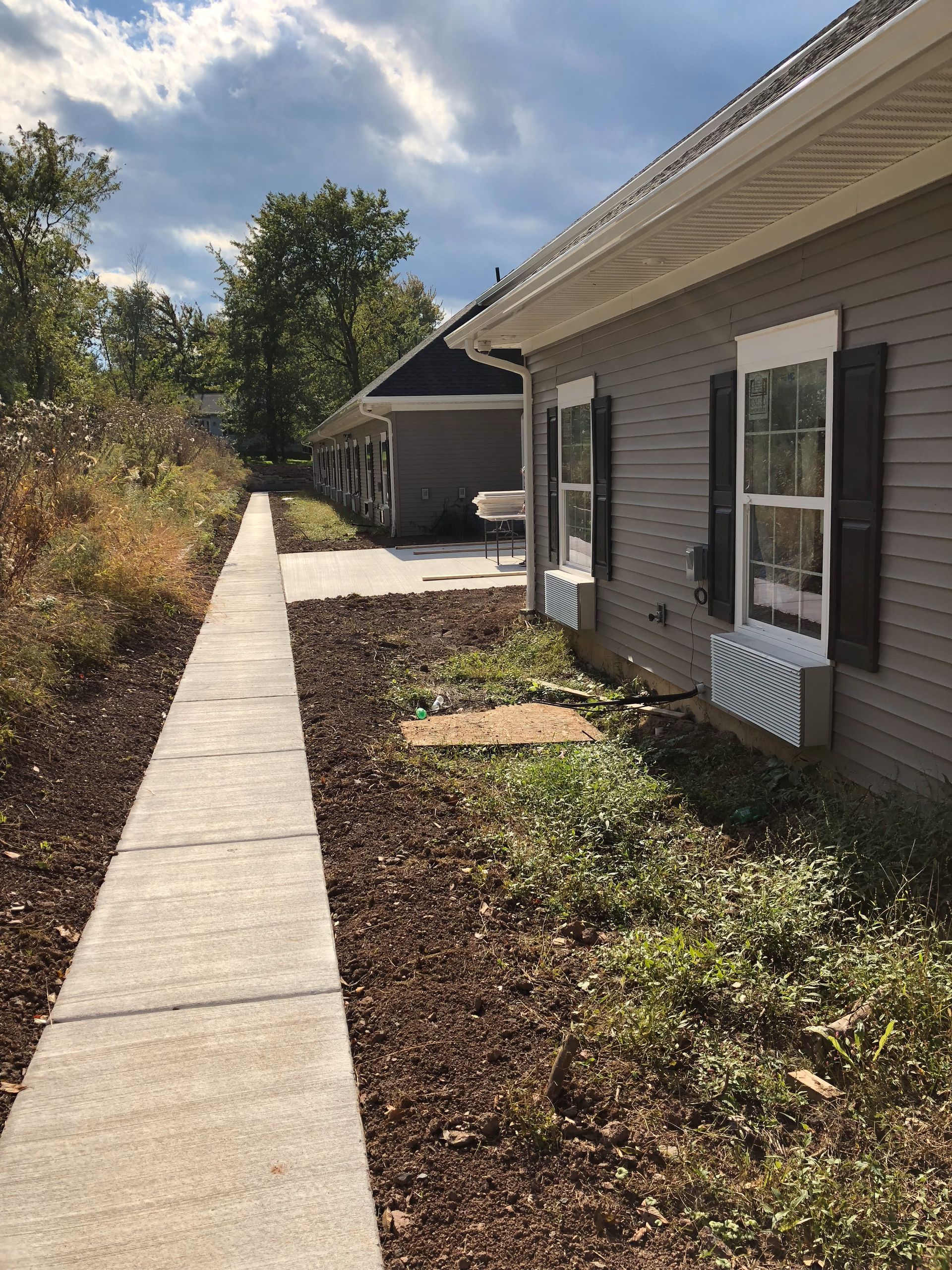 Sidewalk leading to two gray buildings with dark shutters, under a cloudy sky.