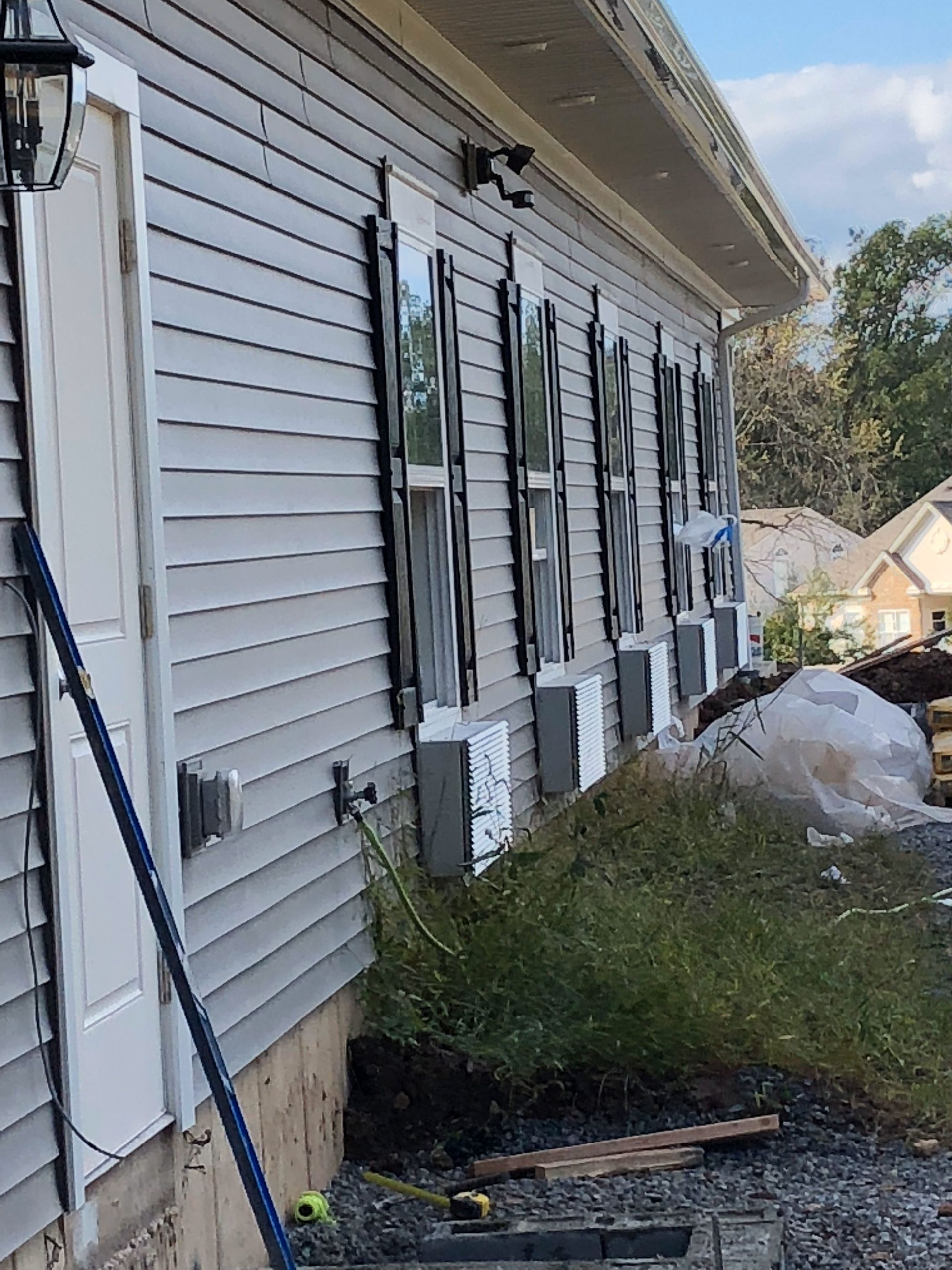 Gray siding on a building with black shutters, visible electrical boxes, and landscaping in progress.