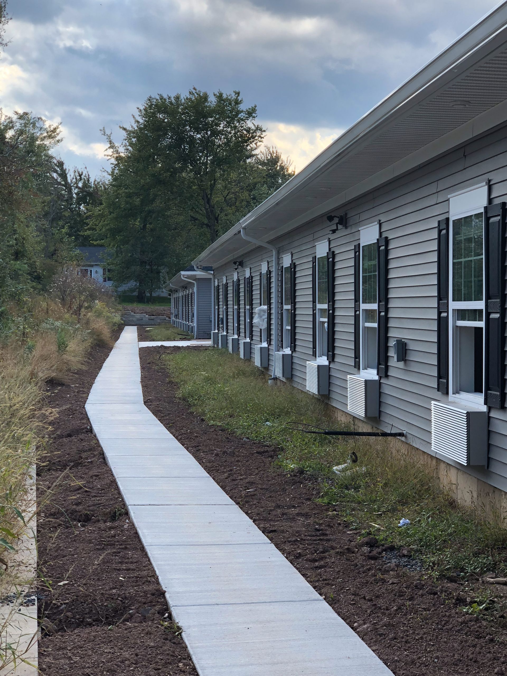 A long concrete sidewalk beside a one-story building with windows and open shutters.