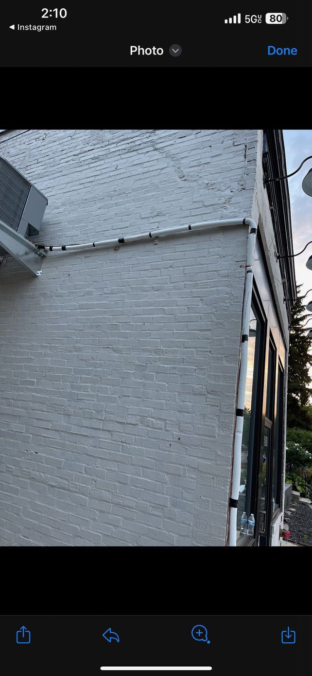 Exterior corner of a building with light gray stucco walls, gutters, and windows.