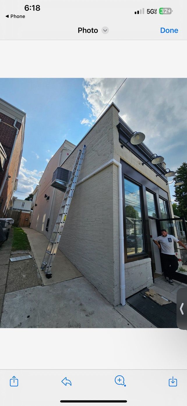 A ladder leaning against a brick building, a person by the entrance, and a blue sky.