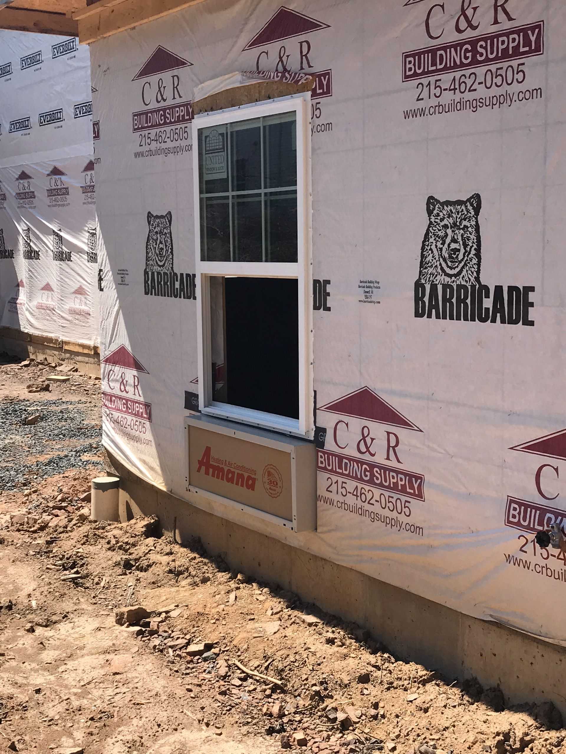 Exterior of a building under construction, with a white-framed window installed. Wrapped in protective sheeting.