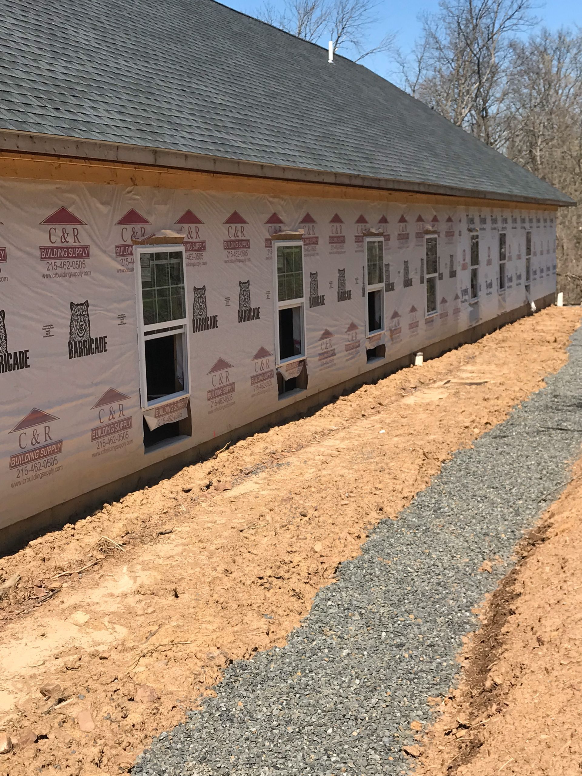 Construction site with windows in a building. Brown dirt, gray gravel path, blue sky.