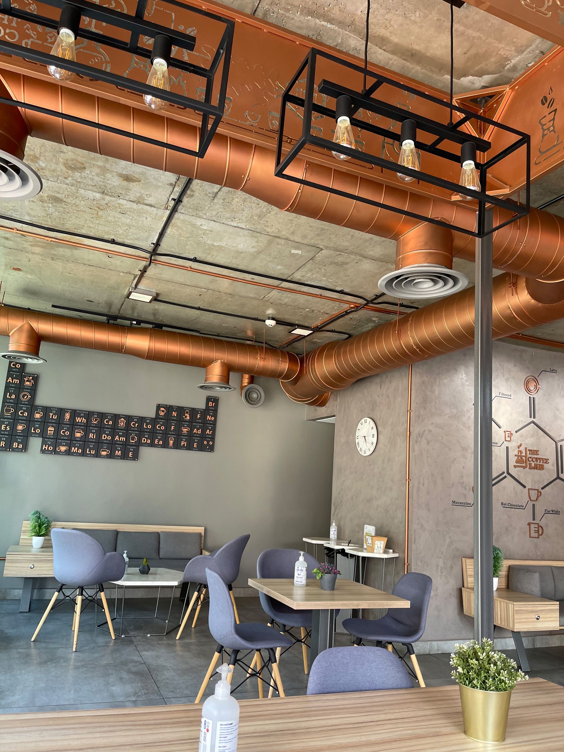 Cafe interior with copper pipes, exposed ceiling, modern furniture. Grey walls, tables, and chairs.