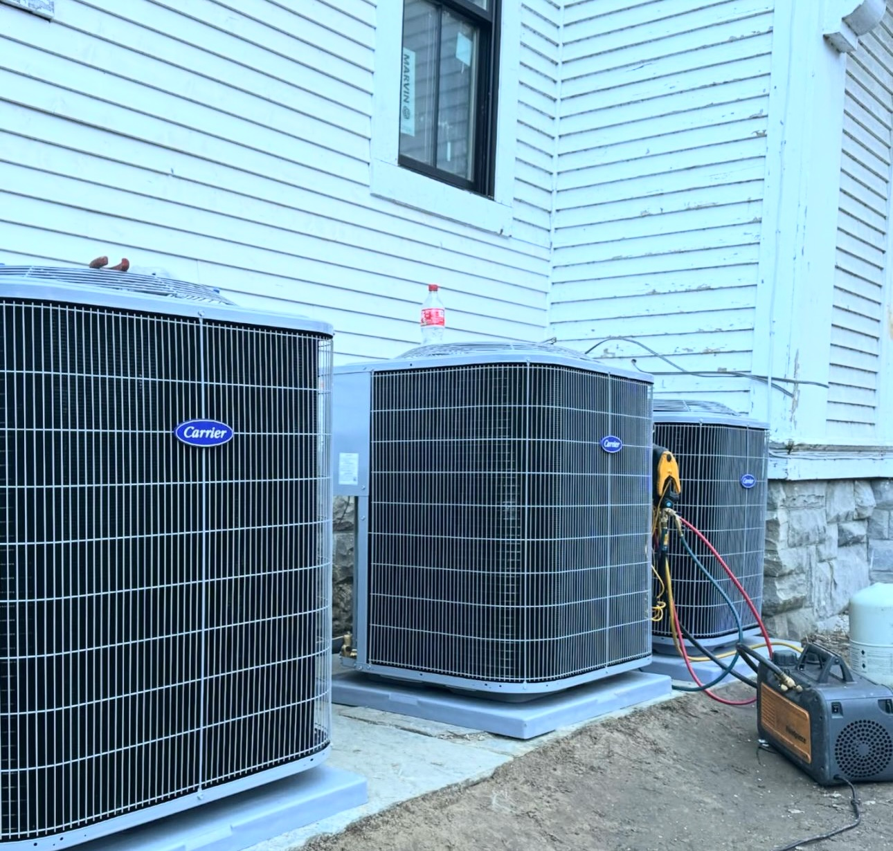 Three Carrier air conditioning units lined up against a white building; vacuum pump on the right.