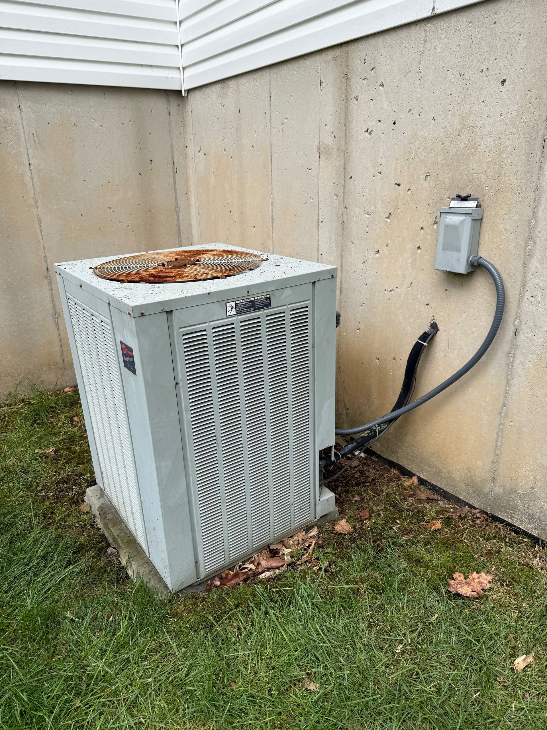 Air conditioning unit outside a building, connected to electrical box. Grassy ground.