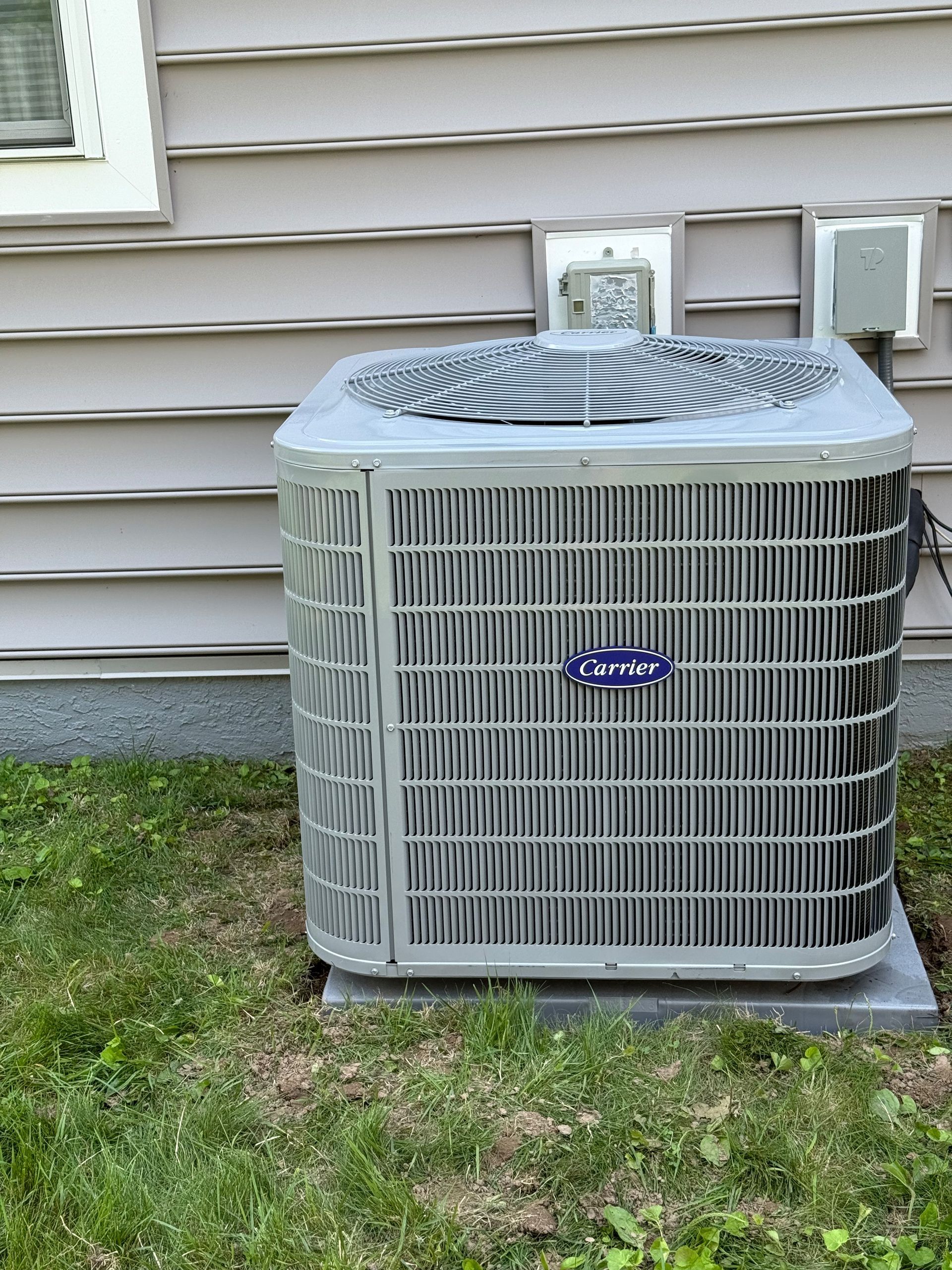 Air conditioning unit outside a house, sitting on concrete, next to green grass.