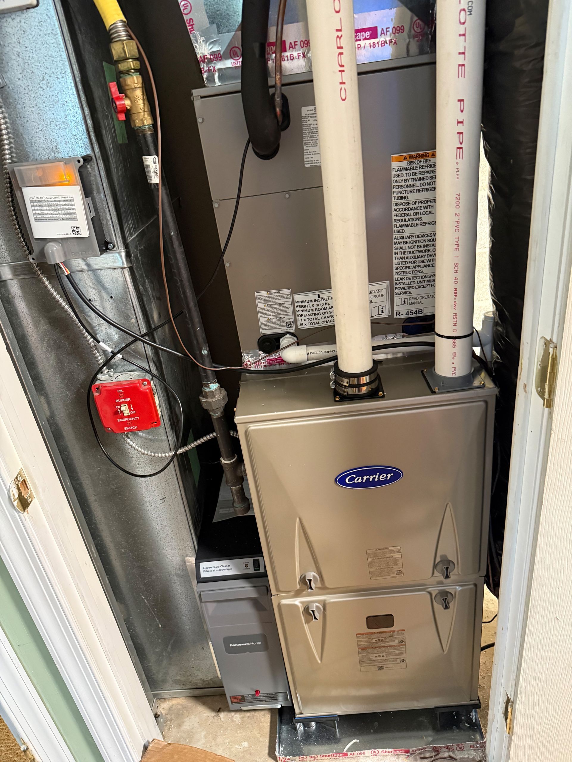A furnace in a utility closet with white PVC pipes, gas valve, and a red carbon monoxide detector.