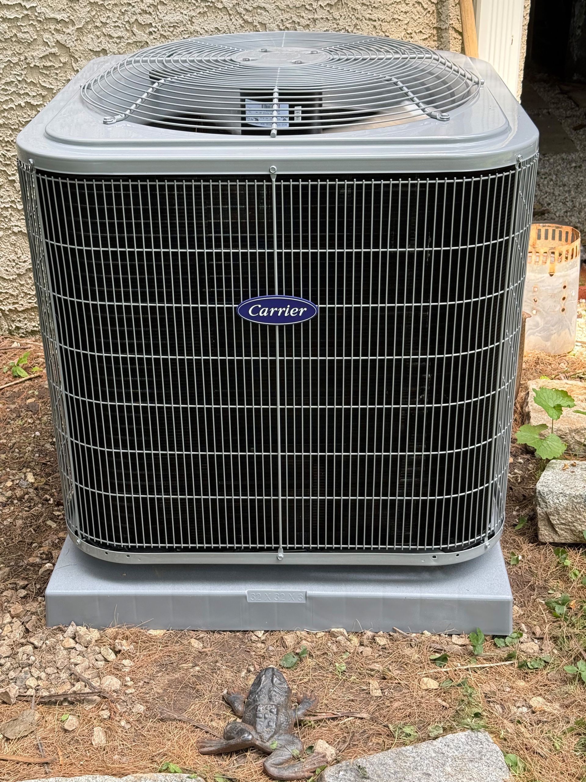 Gray Carrier air conditioning unit on a concrete base, with a decorative lizard in front.