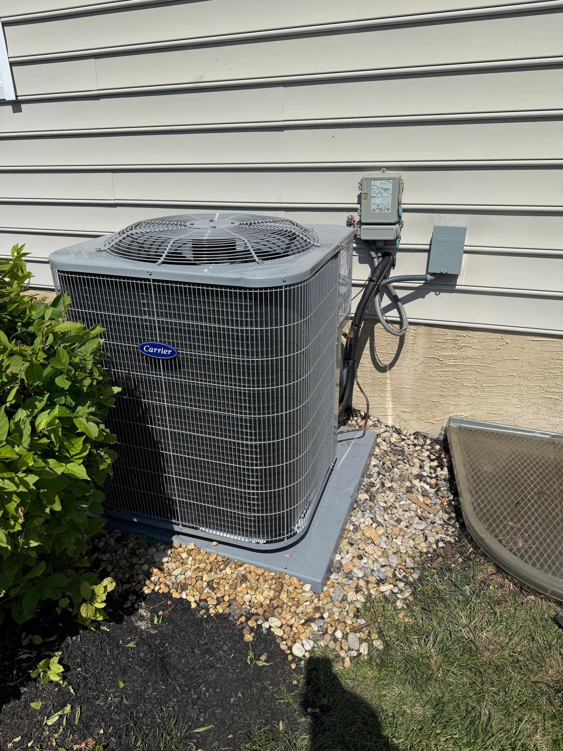 Air conditioning unit outside a house, set on a gray pad in a gravel bed.