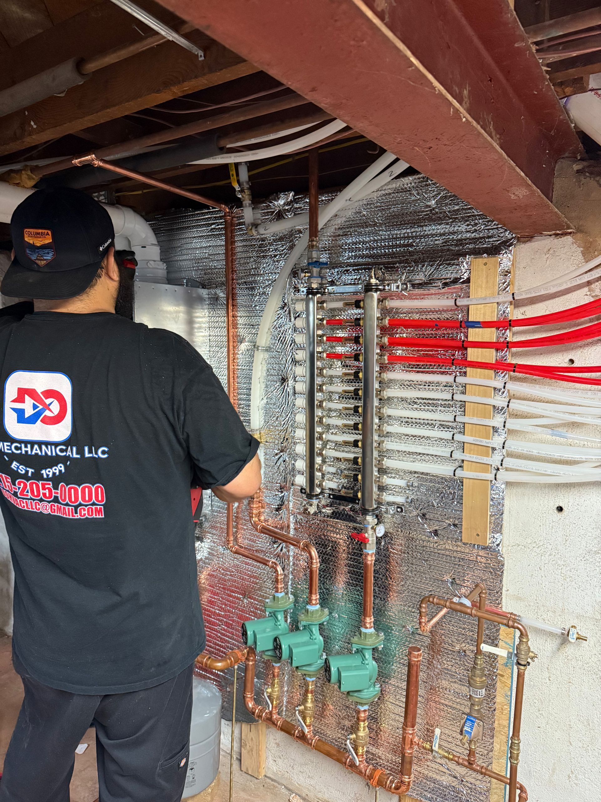 Plumber working on a hydronic heating system in a basement, with copper pipes and red PEX tubing.