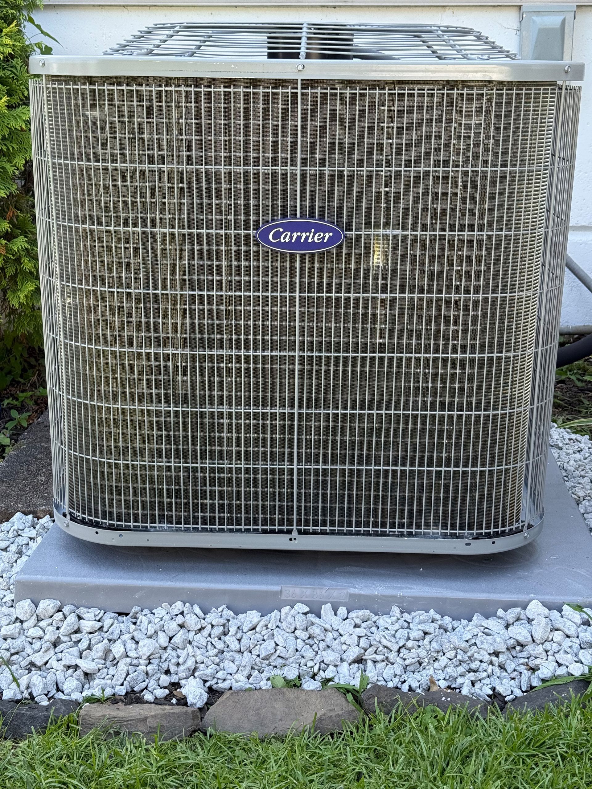 Carrier air conditioning unit, outdoor setting, on concrete base with rock surround.