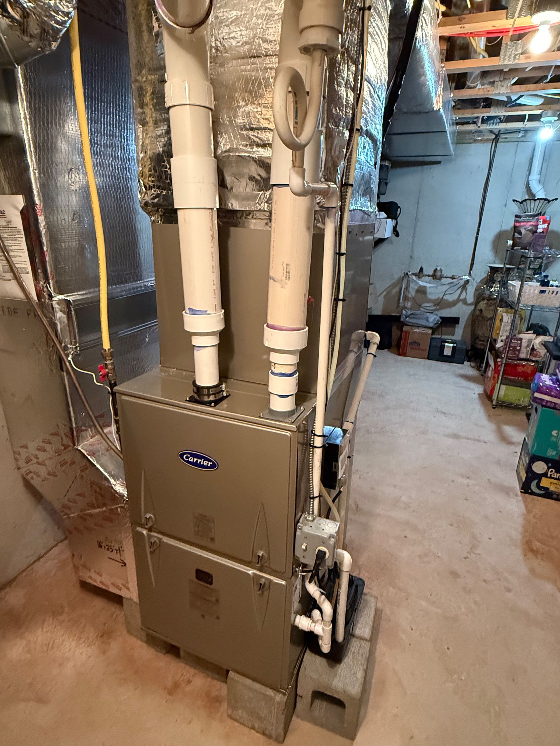 Furnace in a basement, with ducts and PVC pipes. Gray and silver unit on cinder blocks.