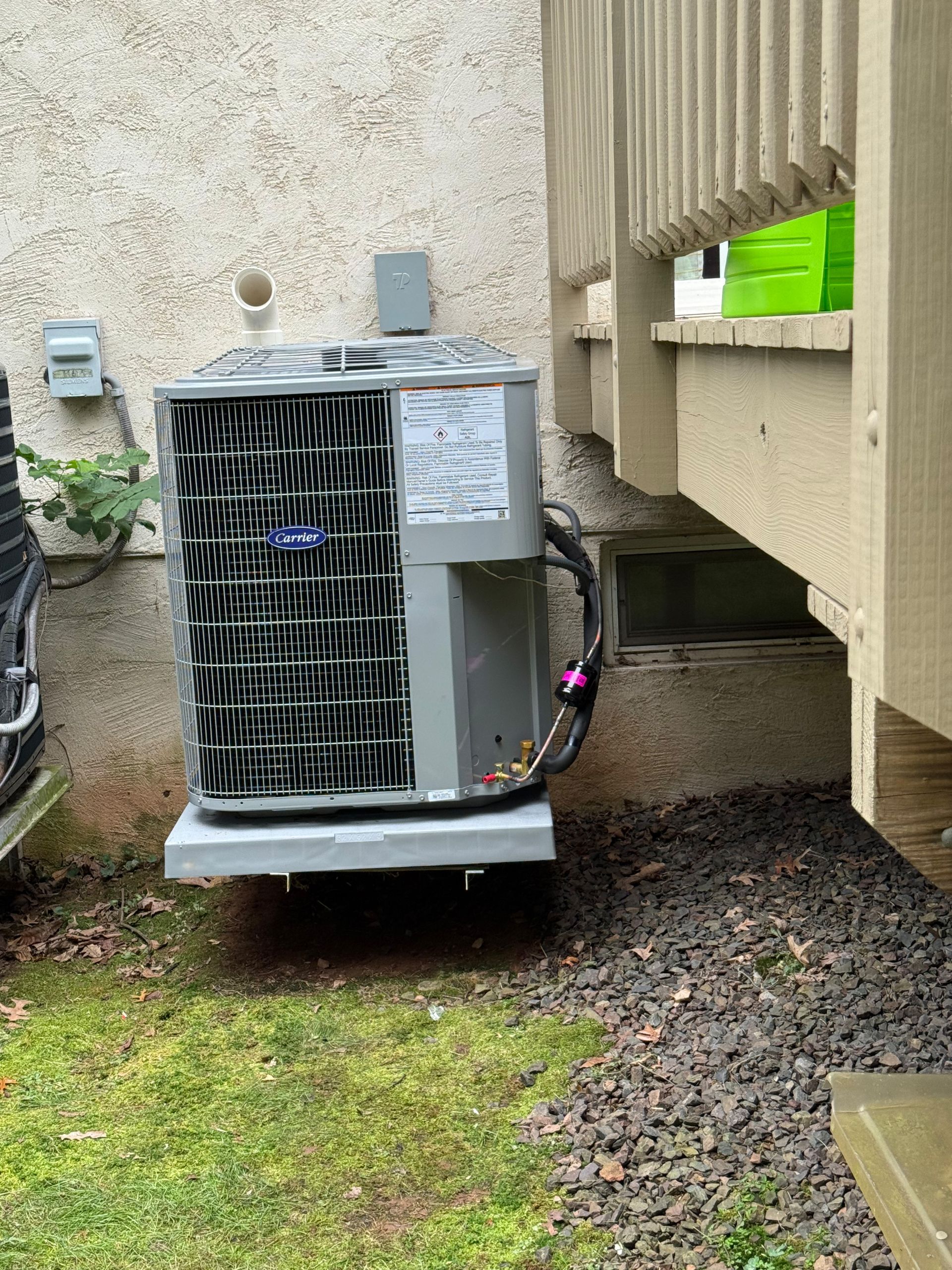 Air conditioning unit mounted on a concrete pad next to a deck, with gravel and grass nearby.