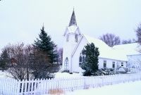 A white church covered in snow with a white picket fence in front of it.